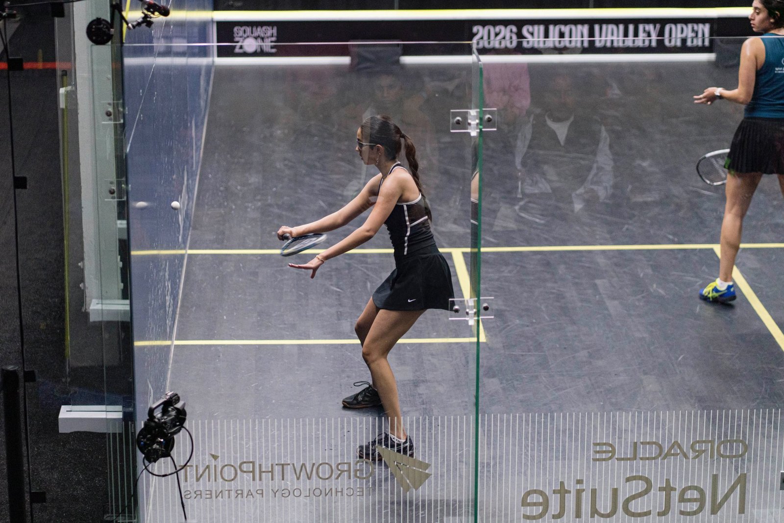 Anahat Singh in a black dress plays a shot on the glass court at the 2026 Silicon Valley Open squash tournament in Redwood City