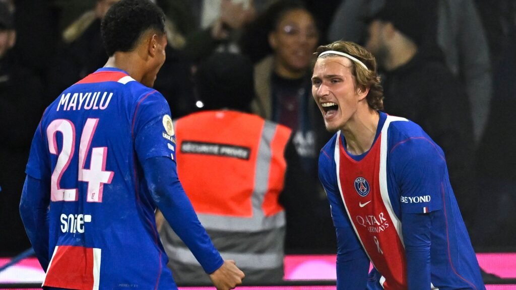 PSG substitutes Senny Mayulu, wearing number 24, and Mika Godts celebrating a goal against Lyon at the Parc des Princes