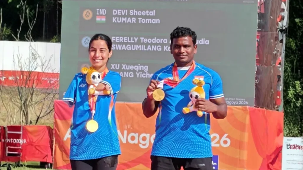 Sheetal Devi and Toman Kumar in India kit holding their compound mixed team gold medals and Games mascots in front of the results board at the Asian Para Games